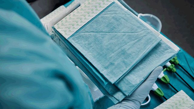 A person wearing a surgical gown and gloves holding various drapes. Photo.