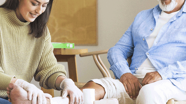 A photo of a nurse tending to a patient's leg in a home environment.